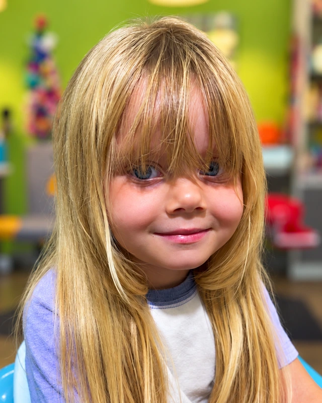 A smiling child with long blond hair and a fringe seated in the salon